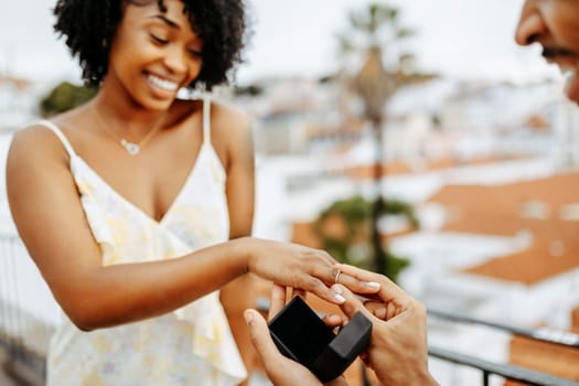 Happy young african american guy put ring on finger of surprised lady, proposes marriage in city