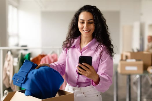 Designer Woman Using Smartphone Packing Garment For Delivery In Store