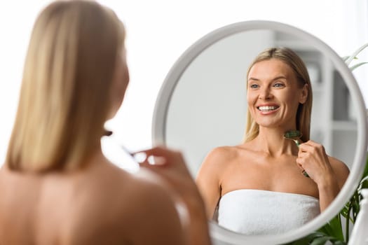 Beauty Treatments. Smiling Mature Woman Using Greenstone Jade Roller At Home, Happy Middle Aged Female Making Body Lifting Massage While Looking At Mirror, Enjoying Selfcare, Selective Focus