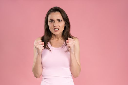 Showing ager beautiful young woman wearing pink t-shirt holding hands gathered in fists, Female half-length portrait. Human emotions, facial expression concept