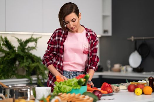 Cutting fresh vegetables pretty housewife cooking dinner wearing a plaid shirt. Cooking with passion young woman with short hair standing at modern kitchen. Healthy food leaving - concept
