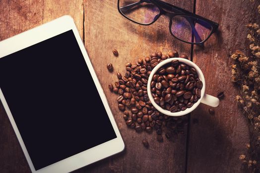 Tablet with coffee beans and glasses on wood table, Vintage color
