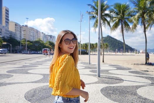 Portrait of smiling relaxed traveler woman walking along Copacabana beach promenade and turns to the camera, Rio de Janeiro, Brazil
