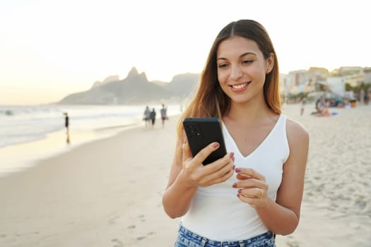 Brazilian young smiling woman on Ipanema holding and watching her smartphone, Rio de Janeiro, Brazil