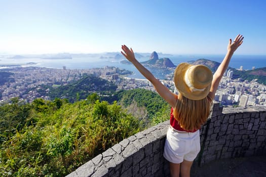 Aerial view of happy young tourist woman with raising arms on belvedere terrace with Guanabara Bay in Rio de Janeiro, Brazil