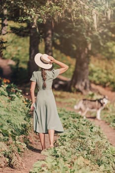 Young woman in straw hat walking with her dog in the forest. Sun summer day with the dog on the way.