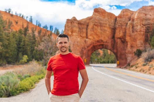 Young caucasian man in background of natural stone arch Bridge in the Red Canyon National Park in Utah, USA
