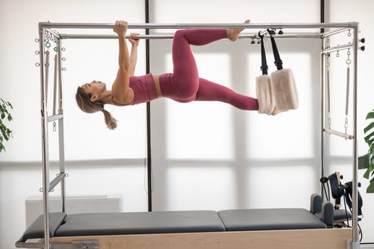 Beautiful asian woman in pink sportswear doing pilates on bed reformer