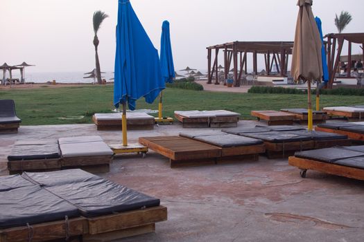 empty sun loungers with a soft surface on the beach. folded umbrellas from the sun. morning at a hotel in Egypt. nobody.