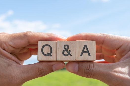 Q and A alphabet on wooden cube in hand hold with background. Question and answer meaning.