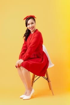 Beautiful young woman posing and looking away with smile while sitting on chair against orange background