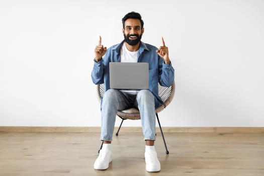 Excited Indian Man With Laptop Pointing Fingers Up Sitting Indoor