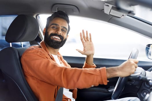 Cheerful Indian Man Gesturing Hi From Driver's Seat In Auto