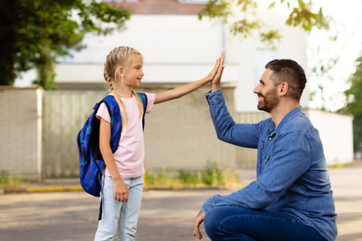 Father-daughter bonding. Parent and pupil of primary school giving high five and smiling at each other