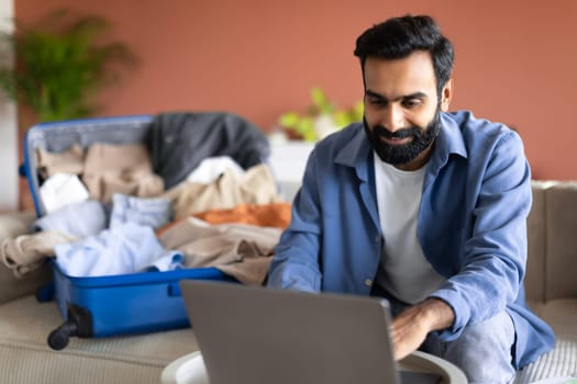 Middle Eastern Guy Using Laptop Booking Tickets Online At Home