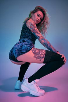 Young fitness blonde woman wearing blue velour booty shorts posing on camera, making squats in studio