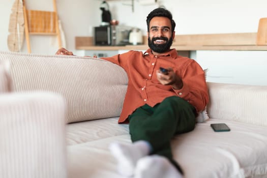 Eastern man with television remote controller watching TV at home