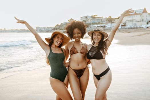 Three diverse girlfriends in swimwear having fun at the beach, women smiling cheerfully while embracing