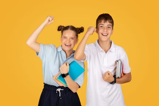 Smiling caucasian teen girl and boy schoolchildren raising hands up, celebrate win and success