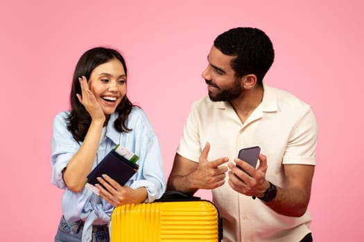 Excited young couple booking tickets online, pink background