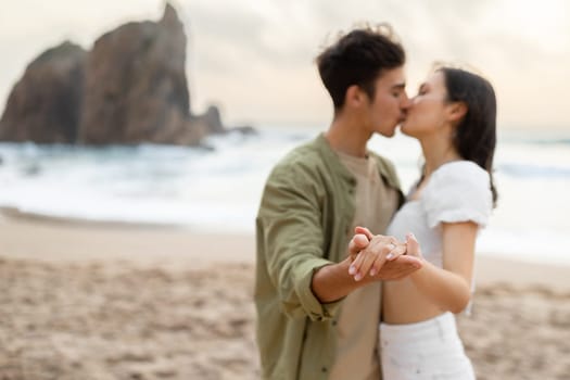 Engaged loving couple enjoying romantic engagement day on the beach, dancing and kissing, focus on hands, free space