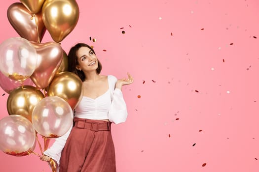 Cheerful millennial caucasian brunette lady with many balloons enjoy confetti