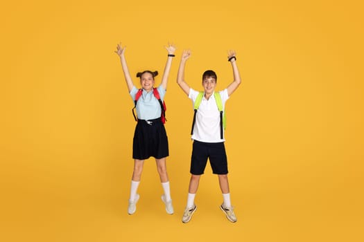 Cheerful caucasian teenager girl and boy pupils with backpacks jumping, freeze in air, celebrating victory