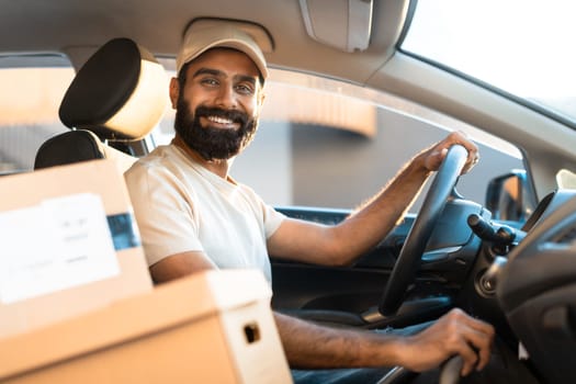 Cheerful Arab Guy Courier Sitting In Car Among Carton Boxes