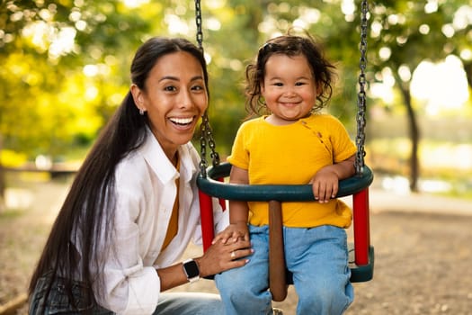 Japanese Mommy And Toddler Daughter Posing On Swings In Park