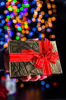 Holding Christmas gift isolated on background with blurred lights. December season, Christmas composition.