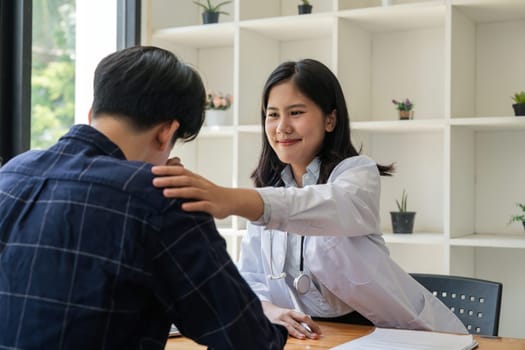 Asian female doctor giving hope and encourage to stressed man patient at hospital. Smiling doctor woman touching on patient shoulder to support take care and helping . Supported and Encouraged