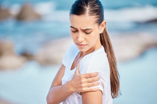 Woman, fitness and arm pain on beach from workout injury, exercise or outdoor accident. Female person with sore shoulder, joint ache or inflammation and muscle tension after exercise on ocean coast