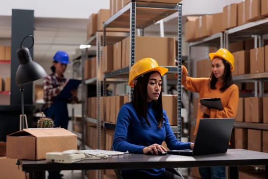 Woman in yellow hardhat working on laptop in warehouse