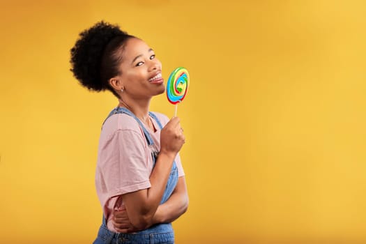 Black woman, portrait and eating candy or lollipop in studio on yellow background and sweets, dessert or food with sugar. Gen z, girl and guilty pleasure in delicious treats, snack or product