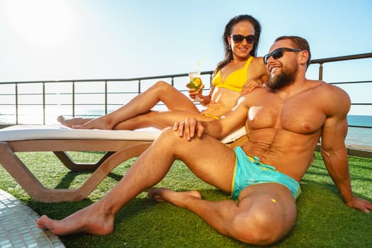 Fit muscular couple in swimwear relaxing near the pool