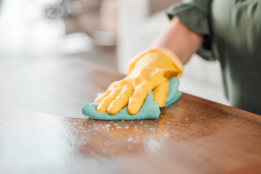 Hands, cleaning and bacteria on a wooden table for hygiene, disinfection or to sanitize a surface in a home. Gloves, spray and product with a woman cleaner in the living room for housework or chores