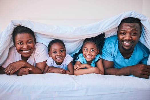 Happy, black family and portrait in a bed with blanket, relax and comfort on the weekend in their home. Face, smile and children with parents in bedroom playing, cover in the morning with fun