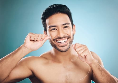 Wellness, teeth and dental floss of a man portrait with cleaning and dental health in a studio. Face, blue background and healthy male person with flossing for mouth hygiene and healthcare with smile.