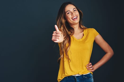 Happy, portrait and a woman with a thumbs up for success, agreement and yes sign. Smile, thank you and a lady with a hand gesture isolated on a dark background in a studio with mockup for motivation