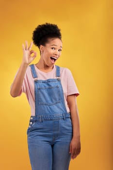 Portrait, okay and hand gesture with an excited black woman in studio on a yellow background. Smile, wow and perfect with a happy young female person showing a sign of support, feedback or review