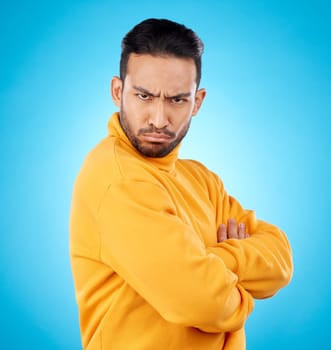 Portrait, frown and asian man with arms crossed in studio angry, frustrated and annoyed on blue background. Conflict, anger and face of Japanese male with defensive body language, denial or offended