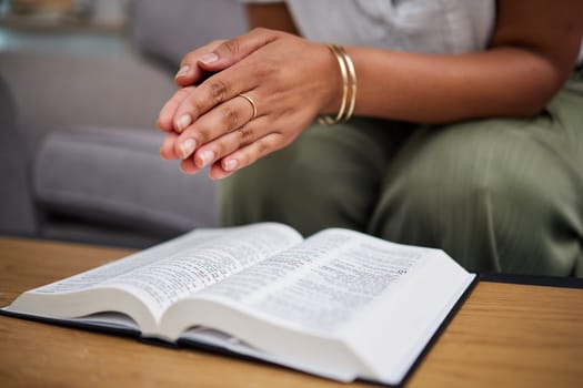 Hands, bible and woman in prayer in home, lounge and reading book of faith, religion and worship study for mindfulness. Person, praying and studying holy book for peace, praise and meditation