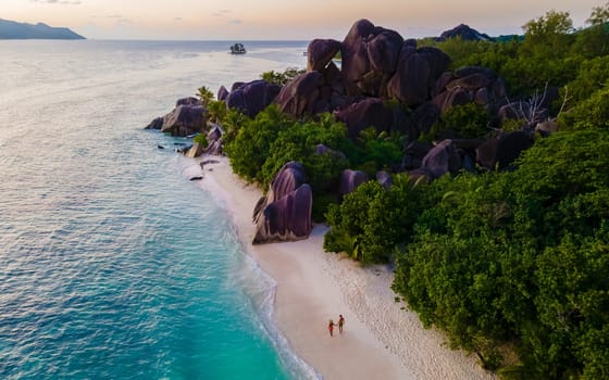 Anse Source d'Argent, La Digue Seychelles, a young couple of men and women on a tropical beach during sunset, drone aerial view