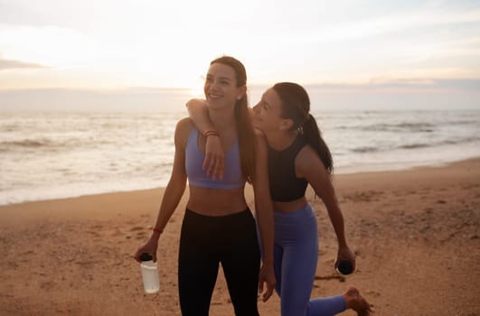 Smiling millennial caucasian twins sisters women hugging, have fun after workout with bottle of water