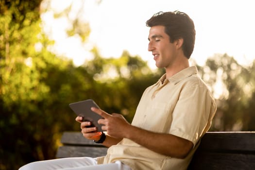 Young man digital nomad sitting on bench, using tablet