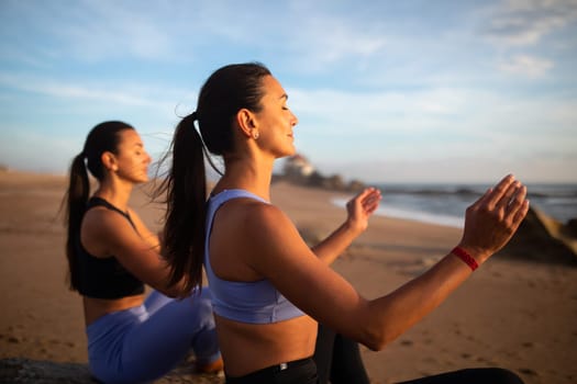 Smiling millennial caucasian twins sisters women practice yoga, enjoy breathing exercises, meditate on sea beach, close up. Morning workout together, health care and lifestyle
