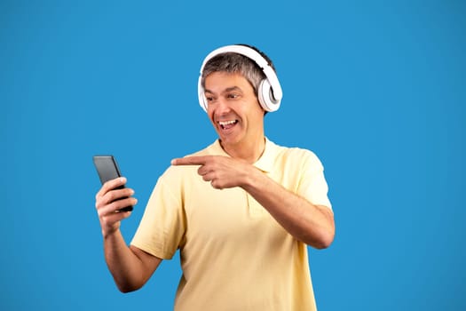 Excited mature man wearing headphones using musical application in studio