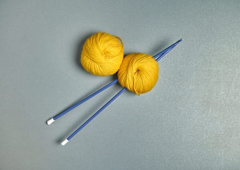 Flat lay of blue spokes and yellow wool yarn on a grey surface