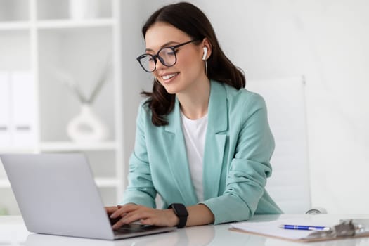 Positive young caucasian business woman in suit, glasses with computer work, enjoys professional occupation