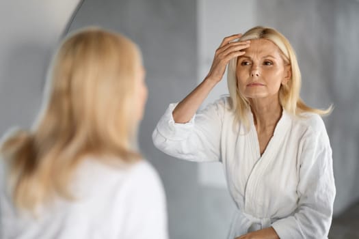 Mature Woman Looking In Mirror And Touching Wrinkles On Her Face,